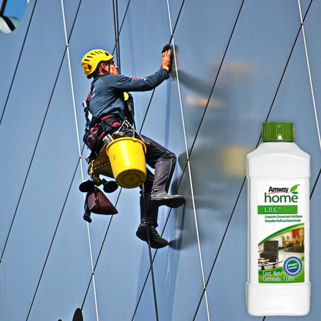 Um homem pendurado limpando os vidor de um prédio com loc multiuso biodegradável da amway